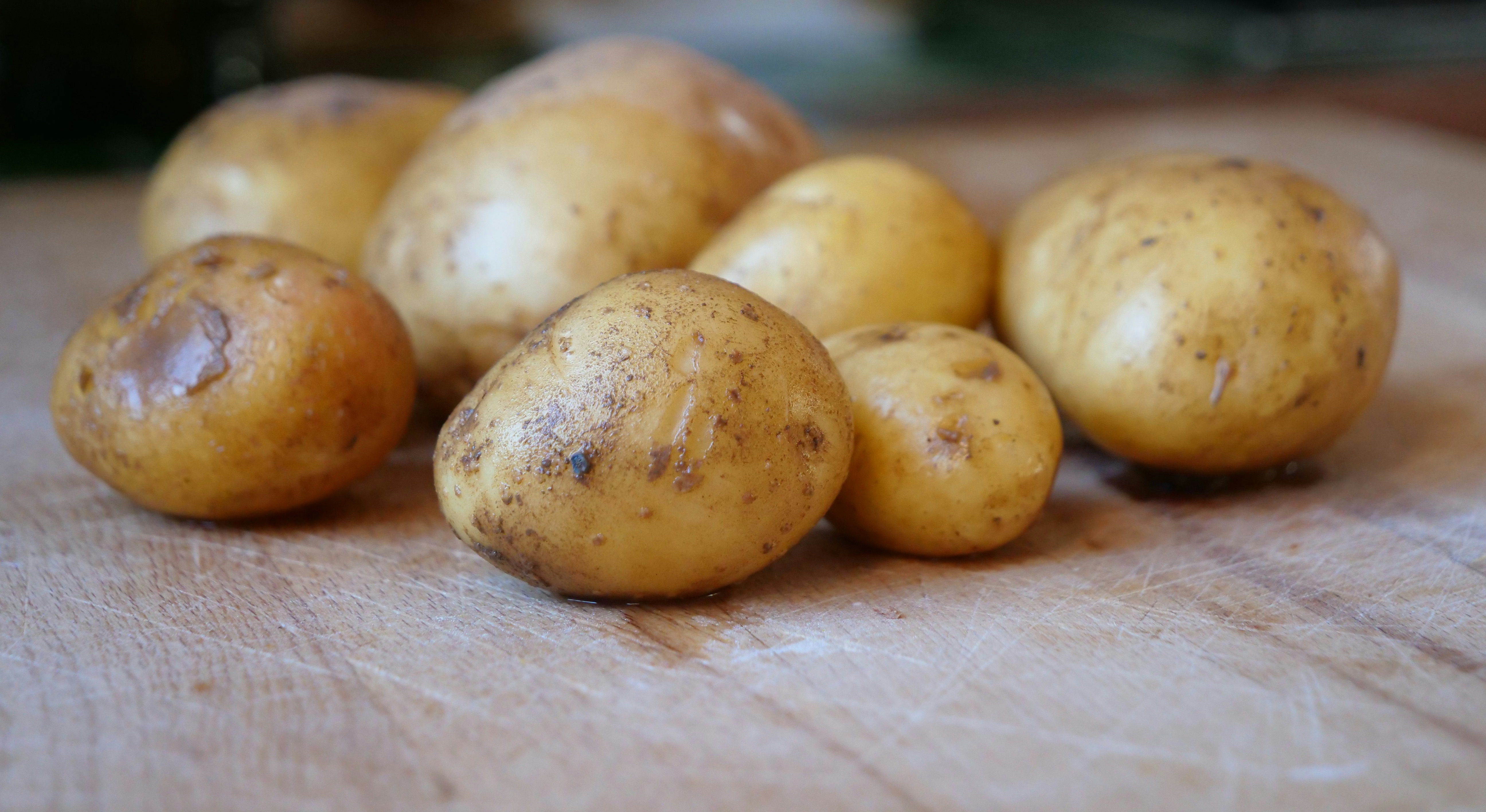 Raw potatoes on a chopping board, ready to be peeled and turned into roast potatoes.